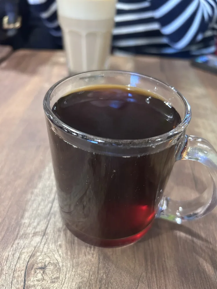 A clear glass mug of black pour-over coffee on a wood table.