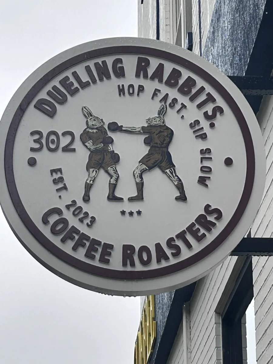 Close-up of the round shop sign with two boxing rabbits, 'Hop Fast Sip Slow,' and 'Est 2023.'